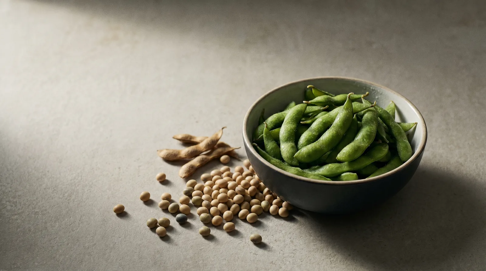 Bowl of green edamame soybean pods beside dried soybeans and pods, the soy hidden in plant protein powders