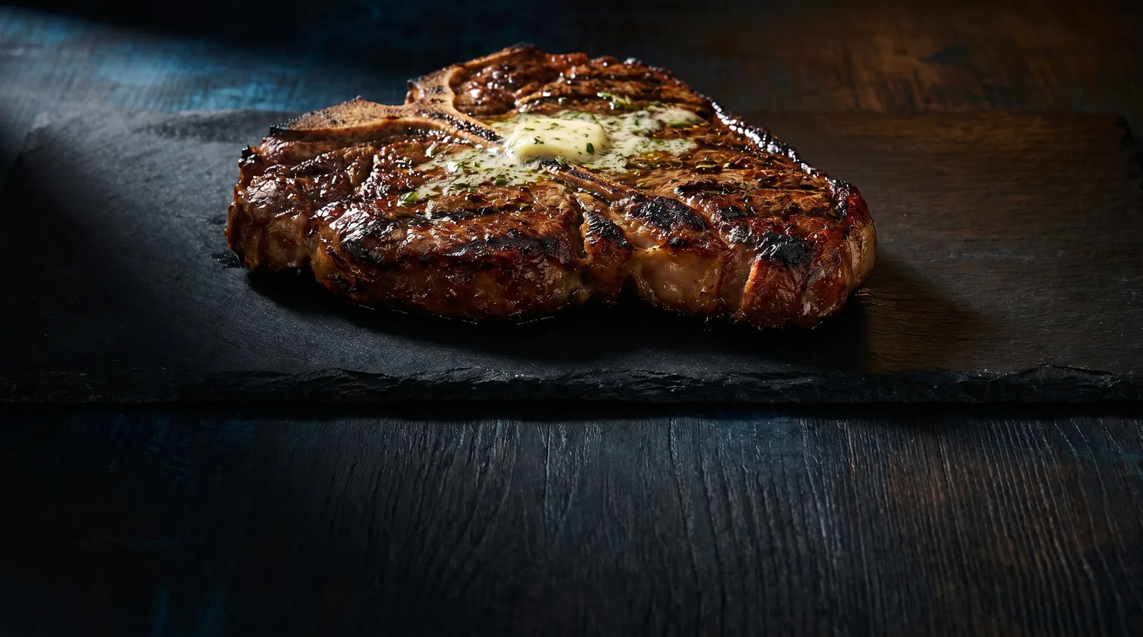 Grilled bone-in T-bone steak topped with herb butter on dark slate, a high-protein single serving