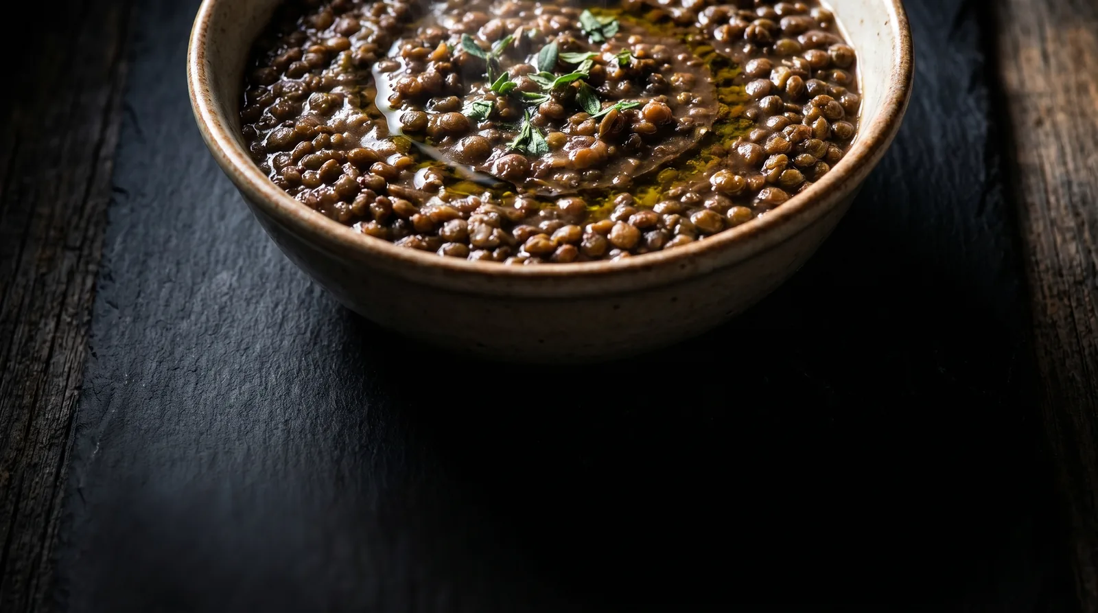Bowl of cooked brown lentils, a high-protein whole-food vegan source, topped with olive oil and thyme on dark wood